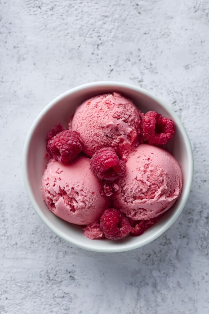 Mary Berry raspberry sorbet scooped into a bowl with fresh raspberries and mint